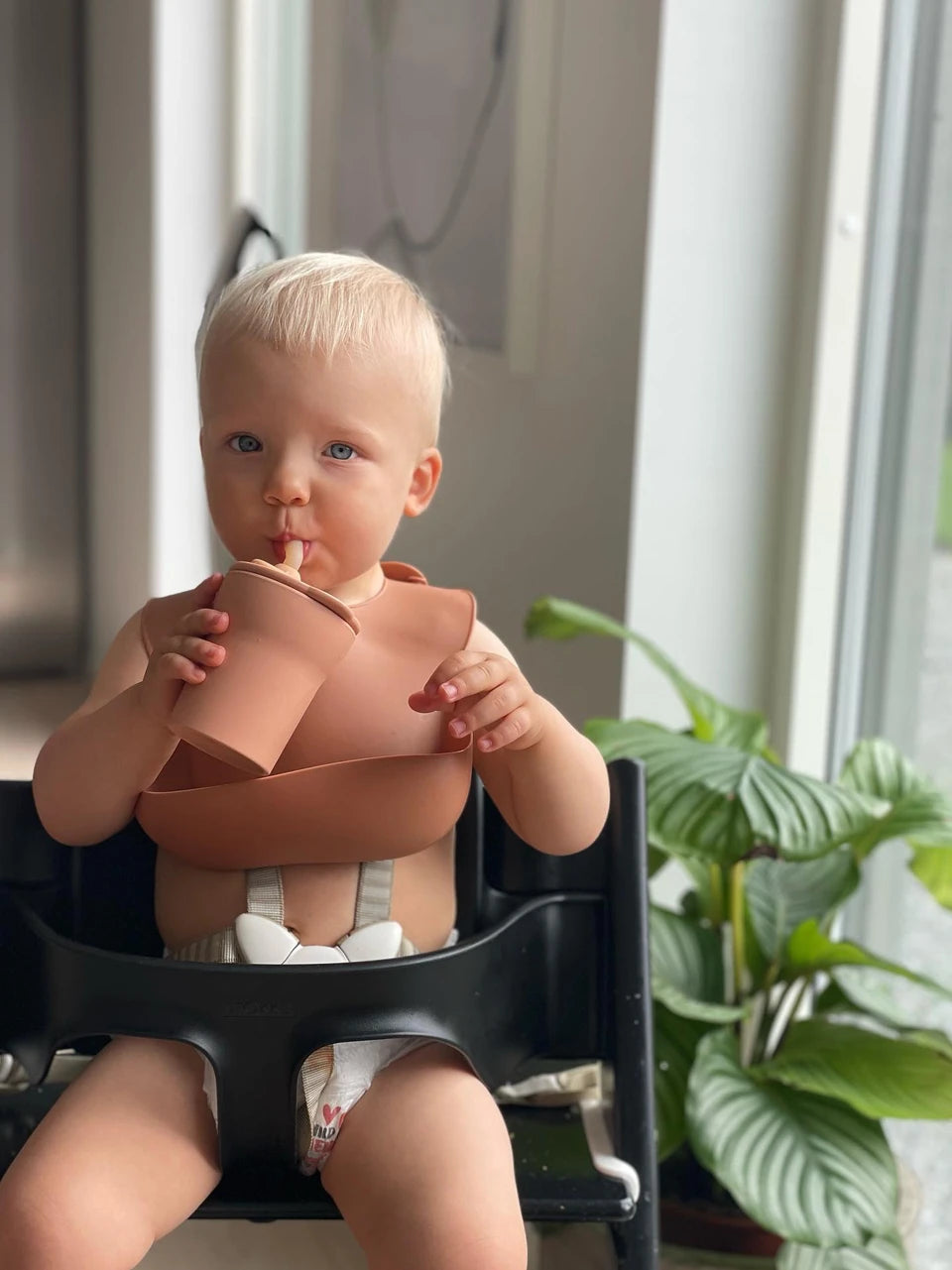 image of child wearing a roll and lock bib, a medical grade silicone baby bib, and drinking from a 1-2-3 sip! cup, an eco friendly sippy cup that adapts to your child as they grow